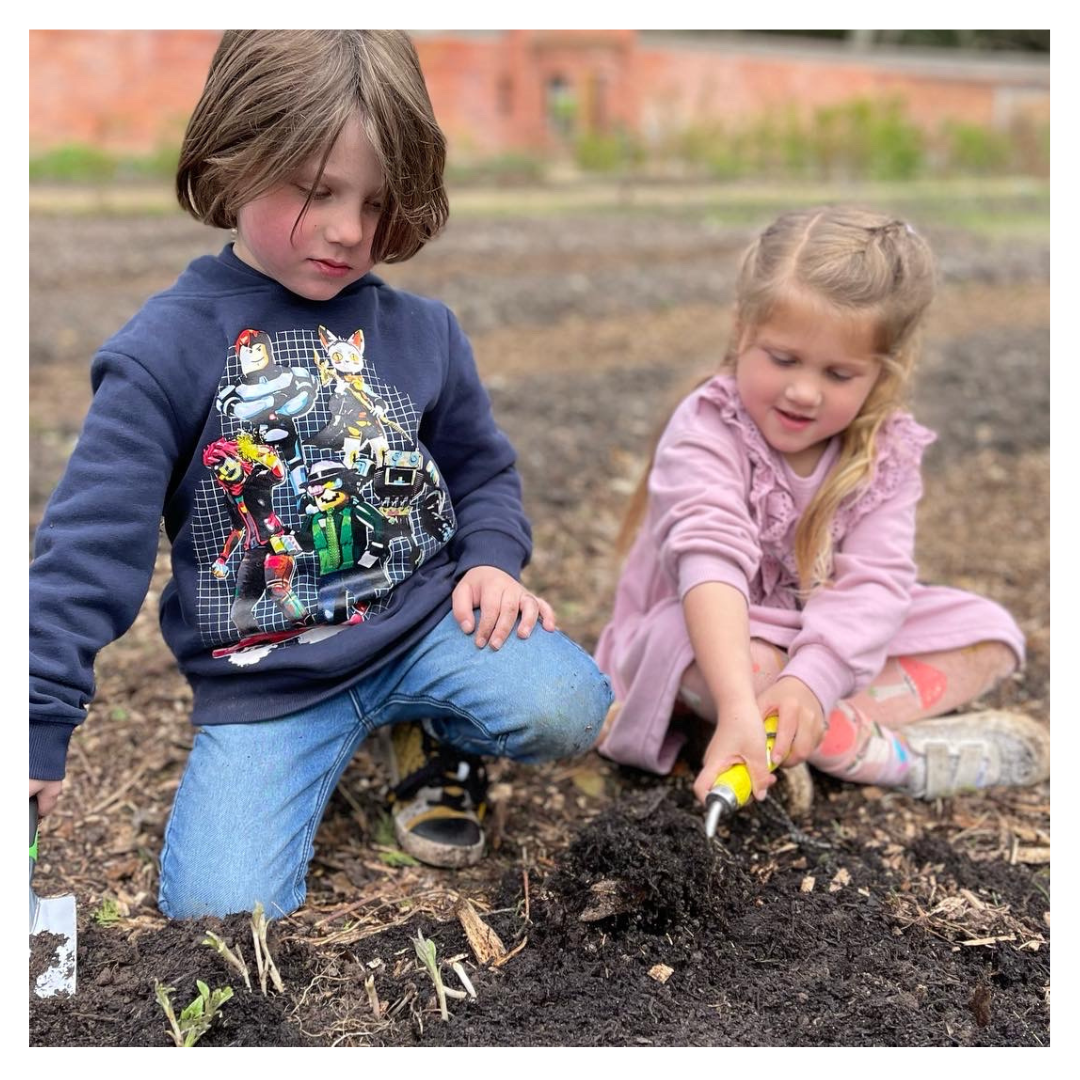 Two children digging soil at Carey’s Secret Garden, engaged in hands-on gardening and outdoor exploration, learning about nature and planting in a vibrant garden setting.